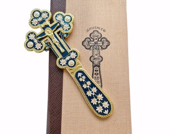 May include: A gold and blue Jerusalem cross with intricate details, including a depiction of Jesus on the cross. The cross is displayed on a brown and beige book with the word "Jerusalem" printed on the cover.