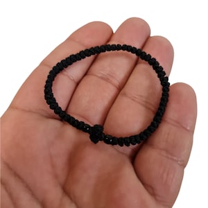 May include: A black knotted bracelet with a small cross charm.