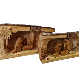 May include: Two wooden nativity scenes carved from tree trunks. The larger scene features a palm tree and the words "Bethlehem" carved into the wood. The smaller scene features the words "Bethlehem" carved into the wood.