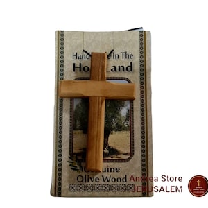 May include: A small wooden cross made from olive wood, handcrafted in the Holy Land. The cross is displayed on a card with the text "Hand Made In The Holy Land" and "Genuine Olive Wood Andrea Store Jerusalem".