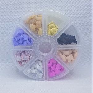 May include: A clear plastic round container with seven compartments, each filled with different coloured incense. The colours are purple, white, pink, orange, yellow, black, and beige.