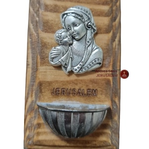 May include: A wooden plaque featuring a silver-toned image of the Virgin Mary and baby Jesus. The plaque has a small metal bowl attached to the bottom and the words "Jerusalem" printed on it.
