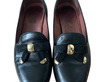 May include: Black leather loafers with gold accents and a black velvet bow on the front.