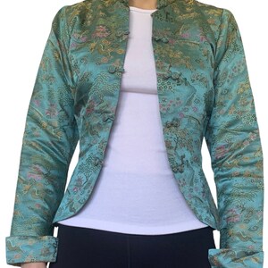 May include: A teal-colored jacket with a mandarin collar and ornate, repeating pattern. The jacket features a button-up front and folded cuffs. The pattern includes trees, buildings, and other Asian-inspired motifs in shades of pink, gold, and green.