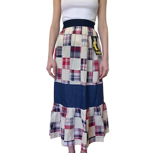May include: A long, patchwork skirt with a denim bottom and a ruffled hem. The skirt is made of a variety of plaid fabrics in red, blue, and white. The skirt has a black elastic waistband.