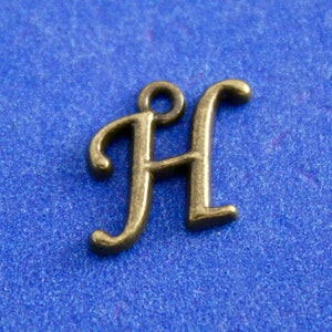 May include: A gold-colored metal charm in the shape of the letter H. The charm is on a blue background.