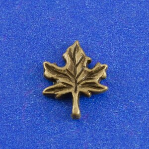 May include: A gold-colored metal maple leaf charm. The leaf is detailed with veins and has a smooth, polished finish.