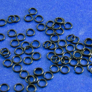 Puede incluir: Una gran cantidad de anillos de salto negros esparcidos sobre una superficie azul. Los anillos son pequeños y circulares, con un acabado liso.
