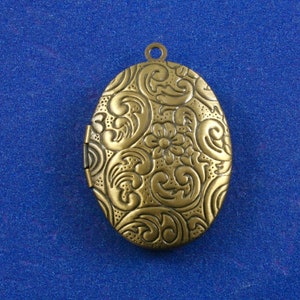 May include: A gold-toned oval locket with an intricate floral design. The locket has a hinged opening and a loop for attaching a chain.