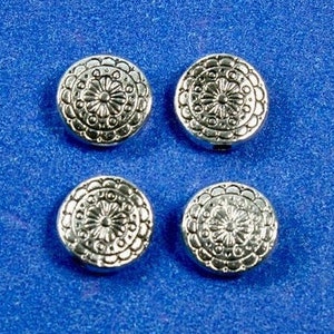 Può includere: Quattro perline rotonde in metallo argentato con un motivo floreale decorativo.