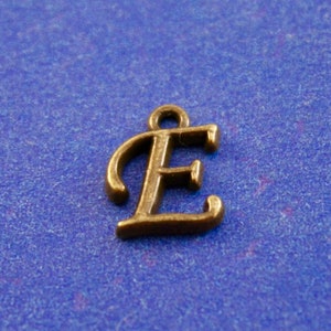 May include: A gold-colored metal charm in the shape of the letter E. The charm is on a blue background.