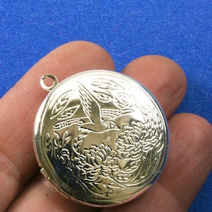 May include: Silver locket featuring an engraved design of a bird flying over flowers.