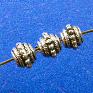 May include: Three silver beads with a textured design are strung on a thin wire. The beads are round and have a raised pattern of small dots.