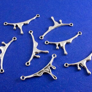 May include: Six silver metal charms shaped like a dripping liquid. The charms have two holes for attaching to jewelry or other crafts.