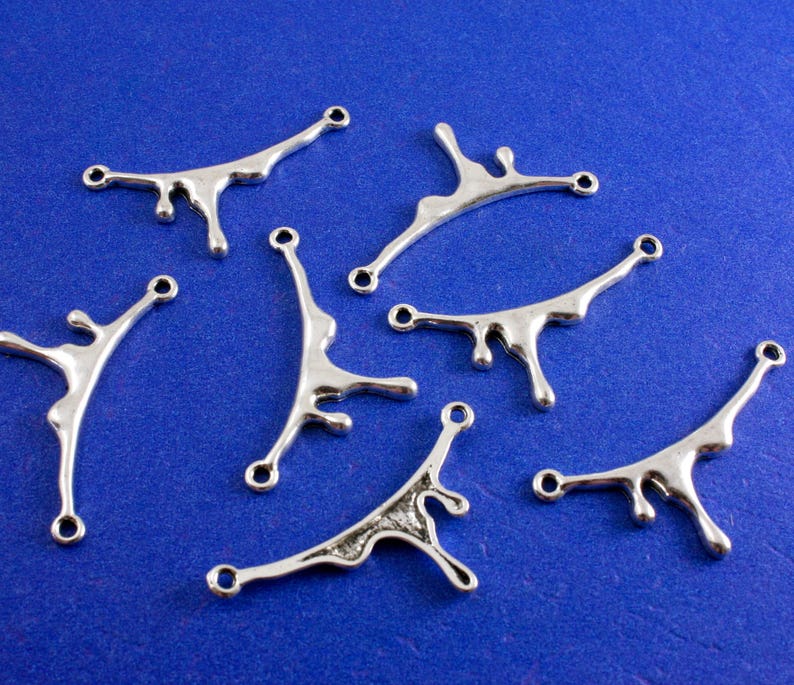 May include: Six silver metal charms shaped like a dripping liquid. The charms have two holes for attaching to jewelry or other crafts.