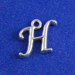 Puede incluir: Encanto de plata en forma de la letra H. La letra está en una fuente cursiva.