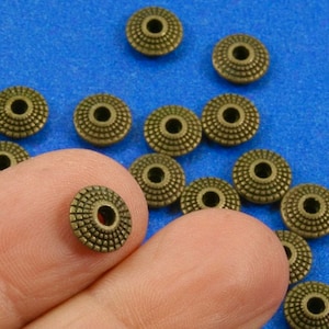 May include: A collection of antique gold-toned metal beads with a textured surface and a small hole in the center. The beads are arranged in a random pattern on a blue surface.