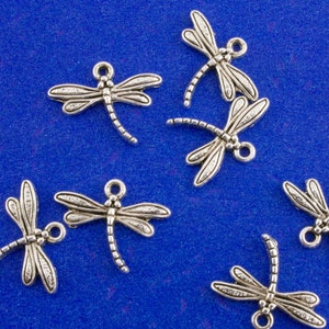 May include: Silver dragonfly charms on a blue background. The charms are detailed and have a textured finish.