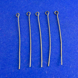 May include: Five gold-colored head pins with a loop at the top, arranged in a row on a blue surface.