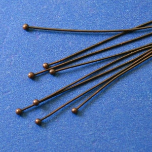 May include: A group of ten copper head pins with rounded tips. The pins are arranged in a fan shape on a blue background.