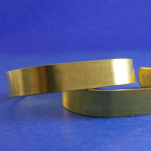 May include: Two gold-colored metal bracelets stacked on top of each other. The bracelets are smooth and have a polished finish.