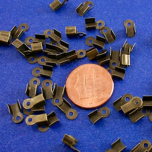 May include: A large quantity of antique gold-toned metal clasps or closures. The clasps are scattered on a blue surface with a US penny in the center.