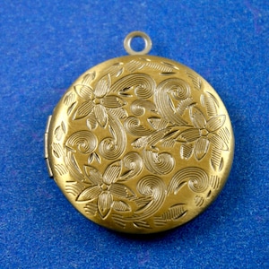 May include: A gold-toned locket with a floral design. The locket has a hinged lid and a loop for attaching a chain.