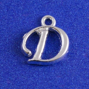 May include: Silver charm in the shape of the letter D. The charm has a loop at the top for attaching to a necklace or bracelet.