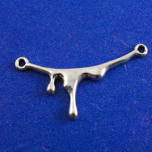 May include: Silver-toned metal charm shaped like a dripping liquid. The charm has two loops for attaching to jewelry or other crafts.