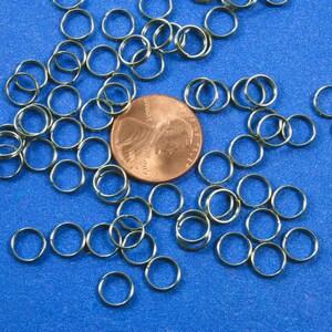 May include: A large quantity of silver jump rings scattered on a blue surface. A US penny is in the center of the image.