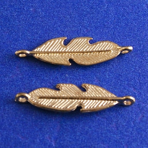 May include: Two gold-colored metal feather charms with a textured surface and a loop at each end.