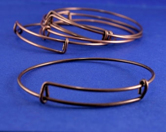 May include: A set of four copper-toned bangle bracelets with a simple, open design. The bracelets are stacked on top of each other on a blue background.