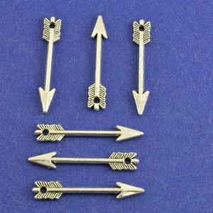 May include: Six silver arrow charms with a pointed tip and a decorative design. The charms are arranged in a row on a blue background.