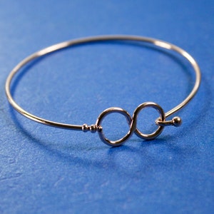 May include: A silver infinity symbol bangle bracelet. The bracelet is made of thin wire and has a simple design.
