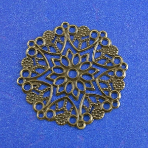 May include: A bronze filigree charm with a circular design featuring a detailed floral pattern. The charm has a hole at the top for hanging.