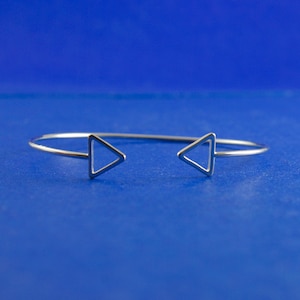 May include: A silver bracelet with two triangle shapes on either end.