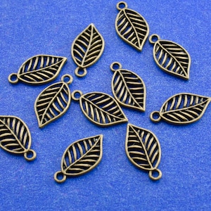 May include: A collection of 12 bronze leaf charms with a delicate, intricate design. The charms have a hole at the top for attaching to jewelry or other crafts.