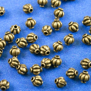 May include: A collection of antique gold metal beads with a textured, fluted design. The beads are scattered on a blue surface.