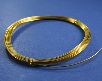Pode incluir: Uma bobina de fio dourado em uma superfície azul. O fio é enrolado em um círculo e tem um acabamento brilhante.