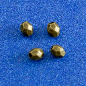 May include: Four antique gold-toned metal beads with a faceted, geometric design. The beads are arranged on a blue background.