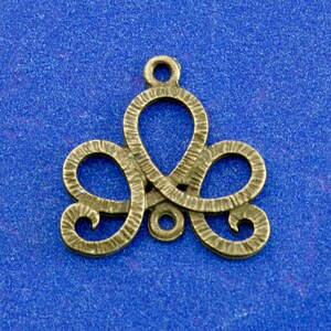 May include: Bronze-colored metal charm with an intricate, swirling design. The charm features a central loop with two curved, symmetrical elements on either side, and a small loop at the top for hanging. The surface has a textured appearance.