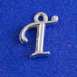 May include: Silver charm in the shape of the letter T. The letter is in a cursive font and has a loop at the top for attaching to a bracelet or necklace.