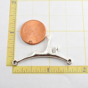 May include: Silver-toned metal pendant shaped like a stylized abstract drip or splash. The pendant has two holes for attaching to a chain or cord. The pendant is about the size of a US quarter.