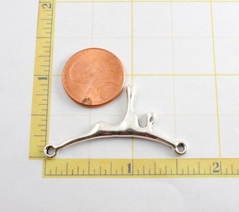May include: Silver-toned metal pendant shaped like a stylized abstract drip or splash. The pendant has two holes for attaching to a chain or cord. The pendant is about the size of a US quarter.