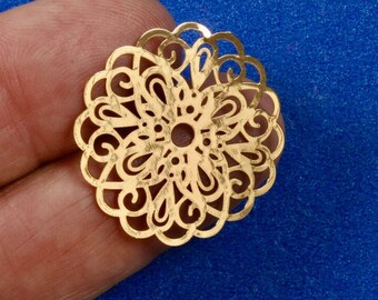 May include: A gold-colored metal filigree charm with a circular design. The charm has a delicate, intricate pattern of swirls and loops.