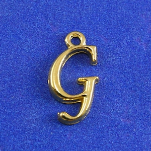 May include: Gold-colored metal charm in the shape of the letter G. The charm has a loop at the top for attaching to a necklace or bracelet.