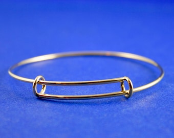 May include: A gold-toned bangle bracelet with a simple, open design. The bracelet is made of a thin, flexible metal and has a spring-loaded clasp.