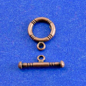 May include: A copper-toned metal clasp with a round ring and a toggle bar. The clasp is a common jewelry finding used for necklaces, bracelets, and other jewelry.