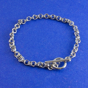 May include: A silver chain bracelet with a toggle clasp. The bracelet is made of small, linked circles.