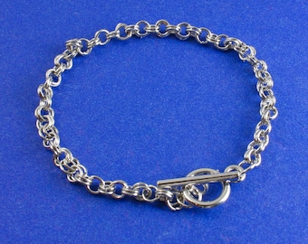 May include: A silver chain bracelet with a toggle clasp. The bracelet is made of small, linked circles.